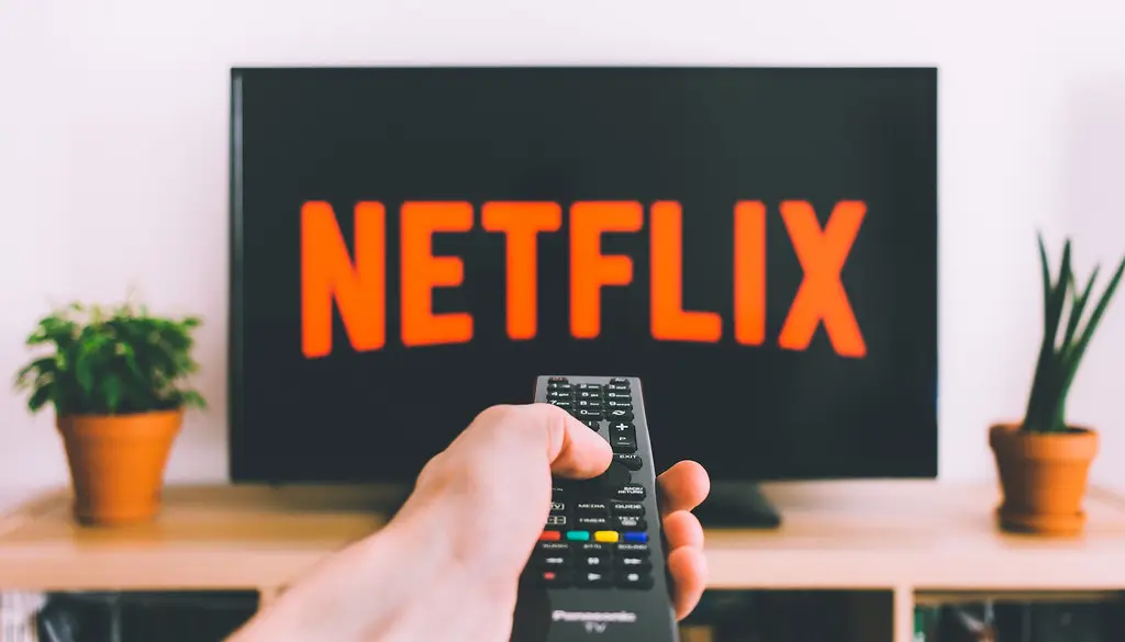 A person holding a streaming device remote in front of a wall-mounted TV