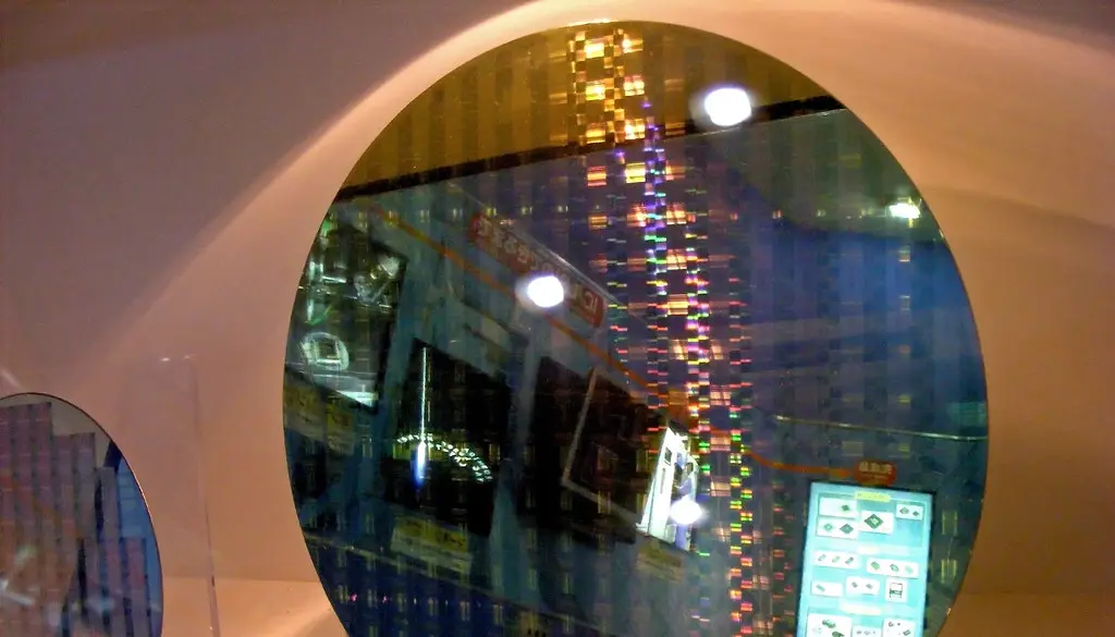 A gloved hand holding a shiny silicon wafer in a semiconductor plant