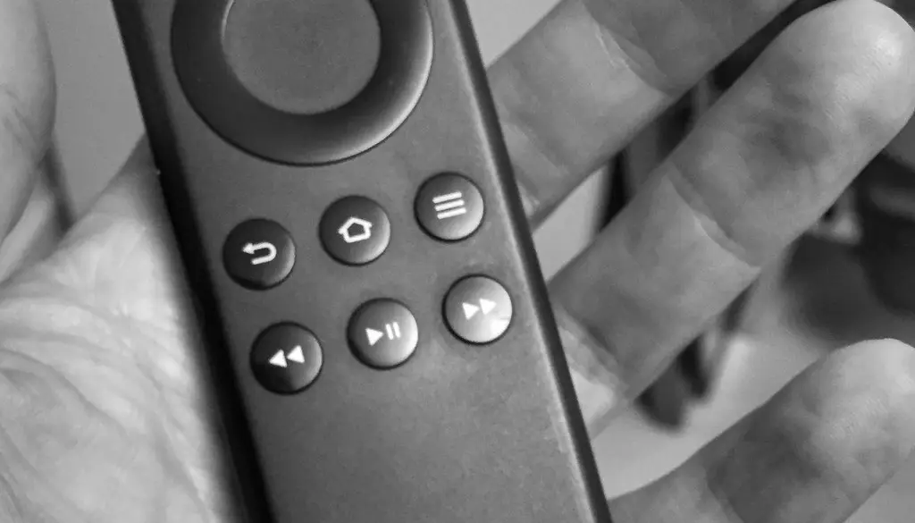 A compact wireless surround speaker on a stand positioned behind a living room couch